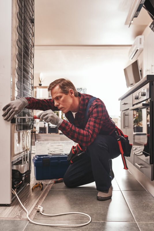 Male technician checking refrigerator with a screwdriver