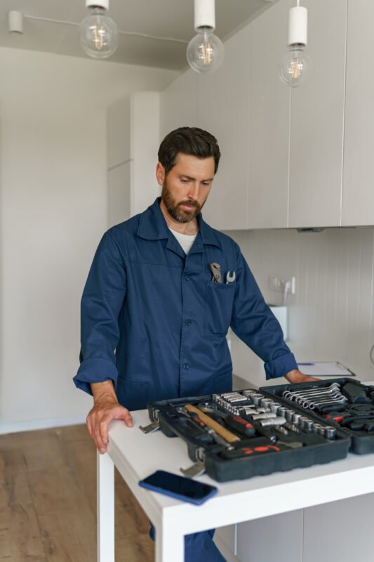 Professional handyman standing on home kitchen and looking on open tool bag with