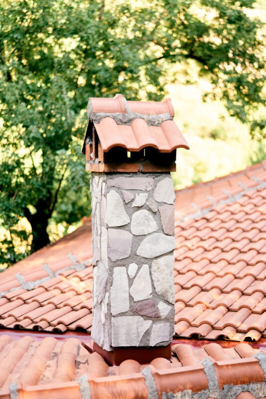 Stone chimney on a tiled roof against a background of greenery