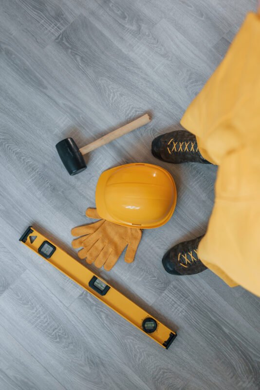 Tools on the floor. Handyman in yellow uniform standing indoors. House renovation conception